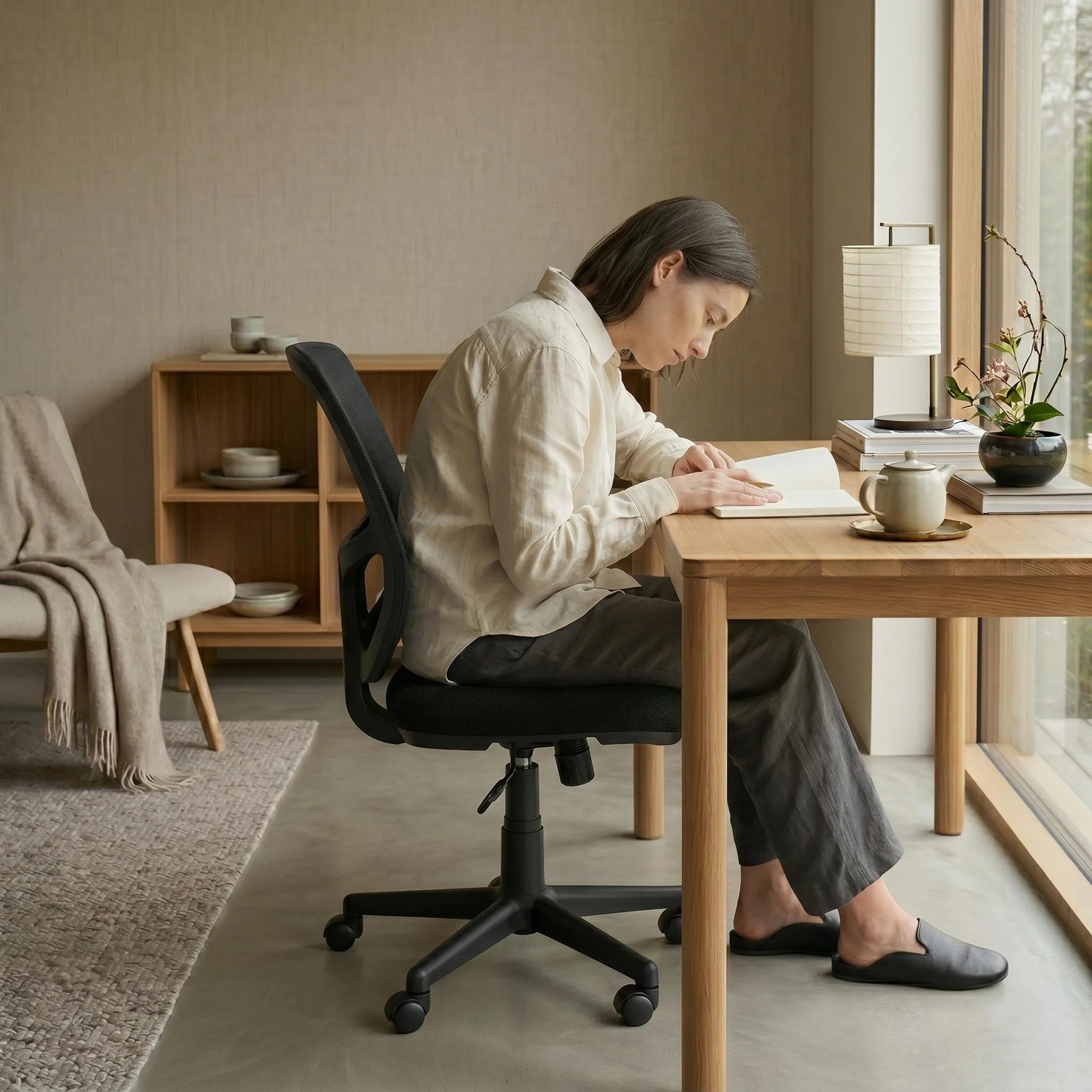 Woman working on a black ergonomic mesh office chair at a wooden desk